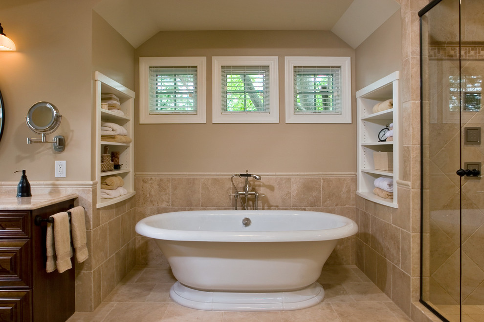 This is an example of a large traditional master bathroom in Boston with a drop-in sink, raised-panel cabinets, dark wood cabinets, granite benchtops, a freestanding tub, an alcove shower, beige tile, porcelain tile, beige walls and concrete floors.