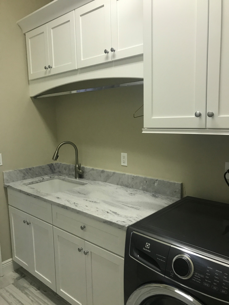 This is an example of a small transitional single-wall utility room in Miami with an undermount sink, flat-panel cabinets, white cabinets, marble benchtops, beige walls, porcelain floors, a side-by-side washer and dryer, grey floor and grey benchtop.