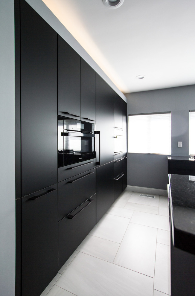 Photo of a mid-sized modern galley open plan kitchen in Philadelphia with an undermount sink, flat-panel cabinets, black cabinets, granite benchtops, grey splashback, stone tile splashback, black appliances, porcelain floors, with island, grey floor and blue benchtop.