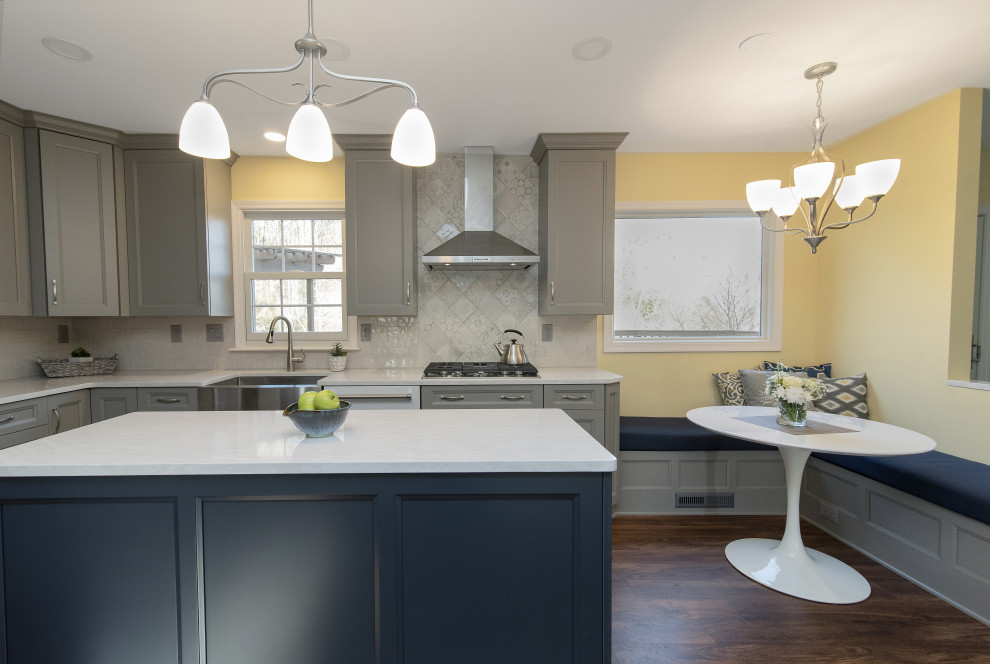 Large transitional u-shaped eat-in kitchen in Baltimore with a farmhouse sink, recessed-panel cabinets, grey cabinets, quartzite benchtops, white splashback, subway tile splashback, white appliances, dark hardwood floors, with island, brown floor and white benchtop.
