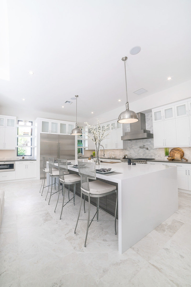 Design ideas for an expansive contemporary l-shaped open plan kitchen in Miami with an undermount sink, shaker cabinets, white cabinets, quartzite benchtops, beige splashback, stone tile splashback, stainless steel appliances, porcelain floors, with island, white floor and black benchtop.