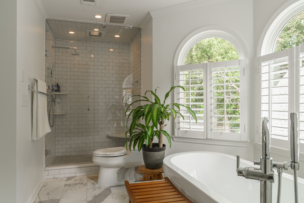 Design ideas for a mid-sized transitional master bathroom in Atlanta with shaker cabinets, white cabinets, a freestanding tub, an alcove shower, a one-piece toilet, white tile, ceramic tile, white walls, ceramic floors, an undermount sink, solid surface benchtops, white floor and a hinged shower door.