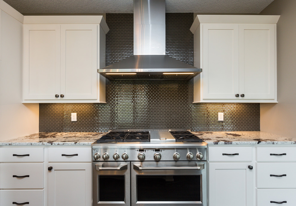 Example of a transitional l-shaped dark wood floor and brown floor kitchen design with an undermount sink, shaker cabinets, white cabinets, granite countertops, gray backsplash, glass sheet backsplash, stainless steel appliances, an island and white countertops