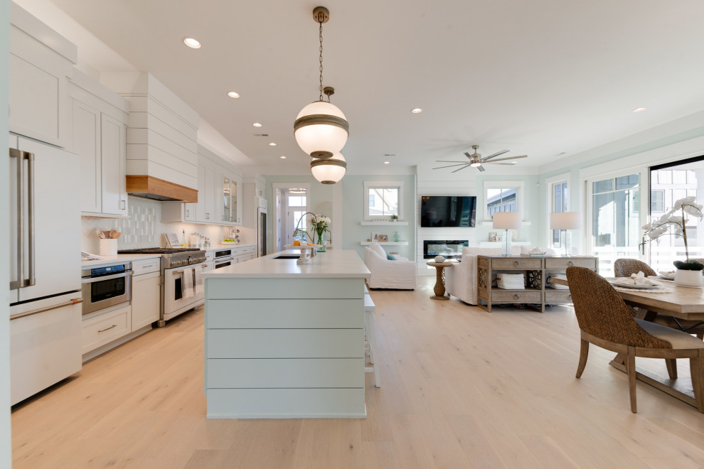 This is an example of a large country galley open plan kitchen in Other with a single-bowl sink, shaker cabinets, white cabinets, quartz benchtops, green splashback, glass tile splashback, white appliances, light hardwood floors, multiple islands, grey floor and white benchtop.