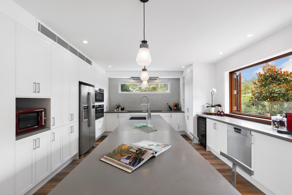 Inspiration for a contemporary u-shaped kitchen in Sydney with an undermount sink, shaker cabinets, white cabinets, grey splashback, stainless steel appliances, dark hardwood floors, with island, brown floor and grey benchtop.