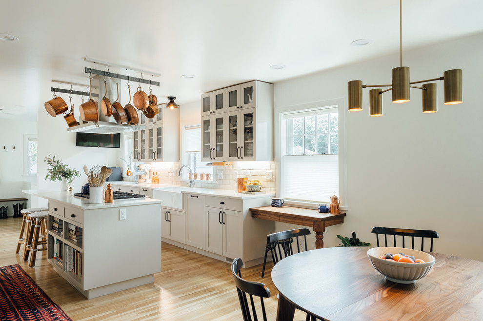 Inspiration for a large transitional galley eat-in kitchen in Salt Lake City with a farmhouse sink, glass-front cabinets, beige cabinets, solid surface benchtops, white splashback, ceramic splashback, stainless steel appliances, medium hardwood floors and with island.