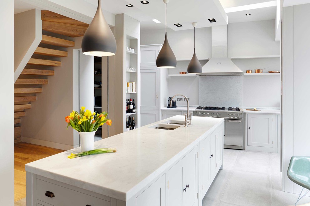 Photo of a large contemporary open plan kitchen in London with a double-bowl sink, shaker cabinets, white cabinets, marble benchtops, stone slab splashback, stainless steel appliances, marble floors, with island and white splashback.