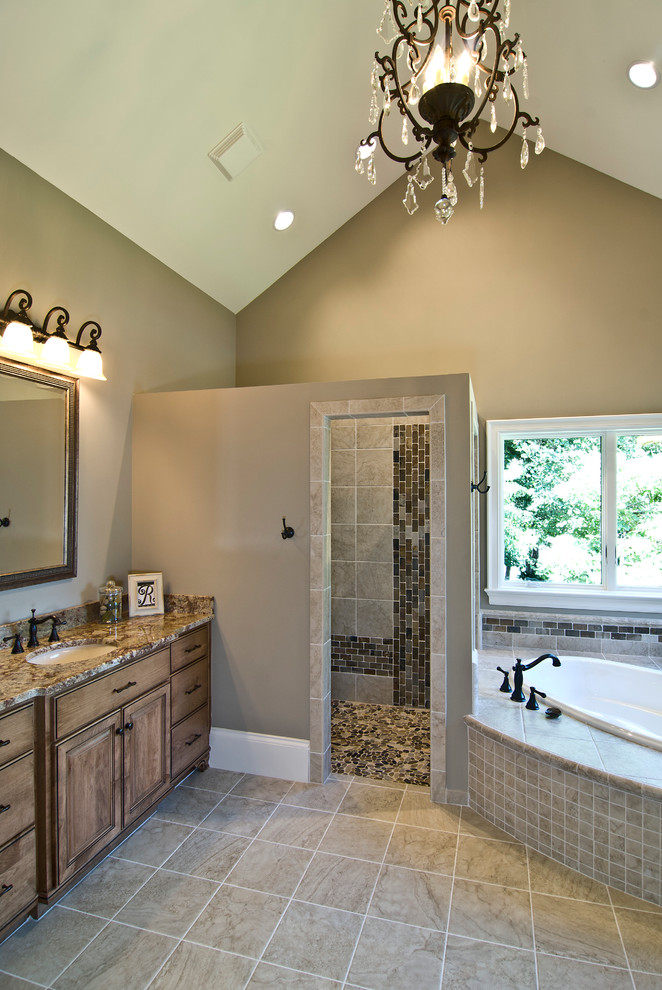 Large transitional master bathroom in Charlotte with raised-panel cabinets, distressed cabinets, a drop-in tub, a curbless shower, a two-piece toilet, brown tile, stone slab, brown walls, ceramic floors, an undermount sink, granite benchtops, beige floor and an open shower.
