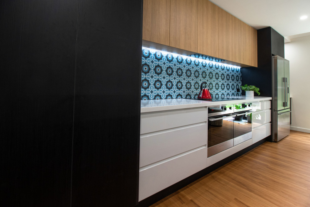 Photo of a large contemporary galley open plan kitchen in Adelaide with a double-bowl sink, flat-panel cabinets, black cabinets, quartz benchtops, blue splashback, cement tile splashback, stainless steel appliances, laminate floors, with island, brown floor, white benchtop and recessed.