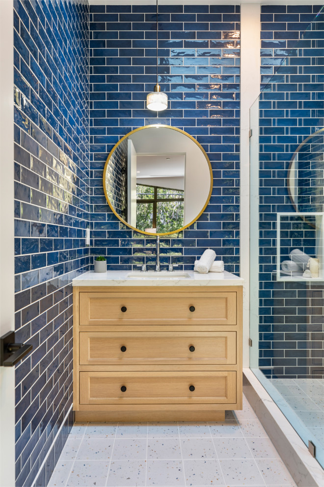 Inspiration for a mid-sized transitional bathroom in Los Angeles with furniture-like cabinets, light wood cabinets, an alcove shower, blue tile, porcelain tile, blue walls, porcelain floors, a drop-in sink, quartzite benchtops, white floor, a hinged shower door, white benchtops, a single vanity and a built-in vanity.