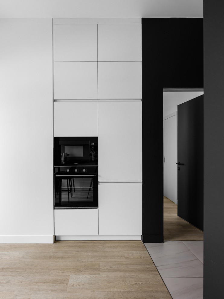 Photo of a small contemporary galley open plan kitchen in Other with a submerged sink, flat-panel cabinets, white cabinets, engineered stone countertops, white splashback, black appliances, laminate floors, no island, beige floors and black worktops.