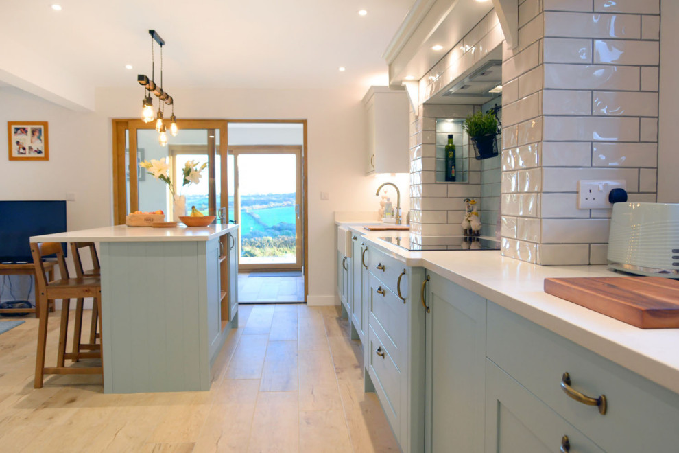 This is an example of a medium sized coastal galley open plan kitchen in Cornwall with shaker cabinets, blue cabinets, quartz worktops, metro tiled splashback, an island and white worktops.