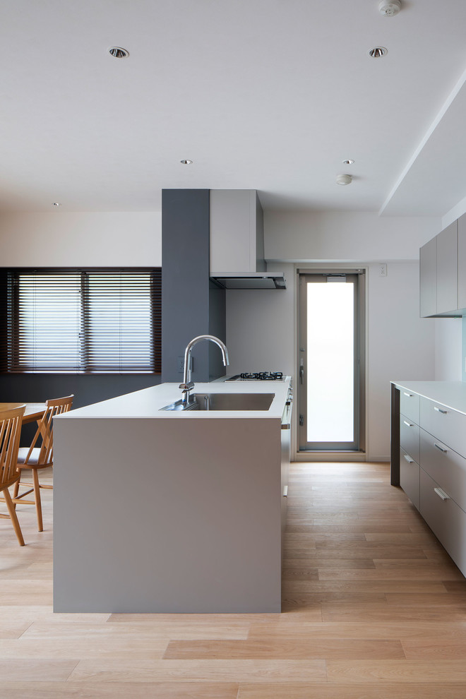 Photo of a small contemporary galley open plan kitchen in Osaka with a drop-in sink, beaded inset cabinets, grey cabinets, laminate benchtops, white splashback, glass tile splashback, plywood floors, with island, beige floor and white benchtop.