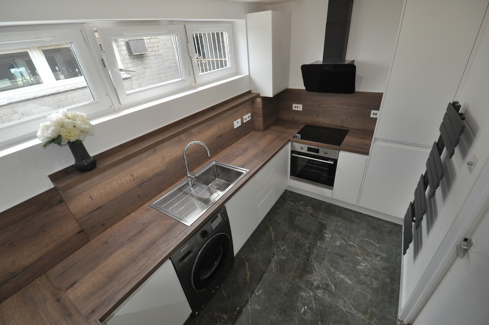 This is an example of a mid-sized contemporary u-shaped separate kitchen in London with a single-bowl sink, flat-panel cabinets, white cabinets, laminate benchtops, brown splashback, black appliances, porcelain floors, no island, green floor and brown benchtop.