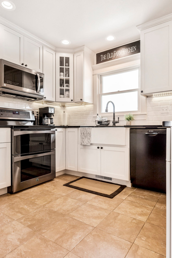 Photo of a small country u-shaped eat-in kitchen in Other with a farmhouse sink, shaker cabinets, white cabinets, quartz benchtops, white splashback, subway tile splashback, black appliances, porcelain floors, a peninsula, beige floor and black benchtop.