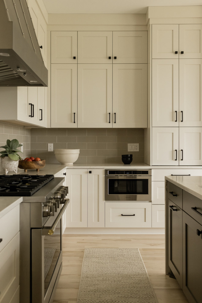Transitional u-shaped light wood floor eat-in kitchen photo with an undermount sink, recessed-panel cabinets, beige cabinets, quartz countertops, gray backsplash, ceramic backsplash, stainless steel appliances, an island and white countertops