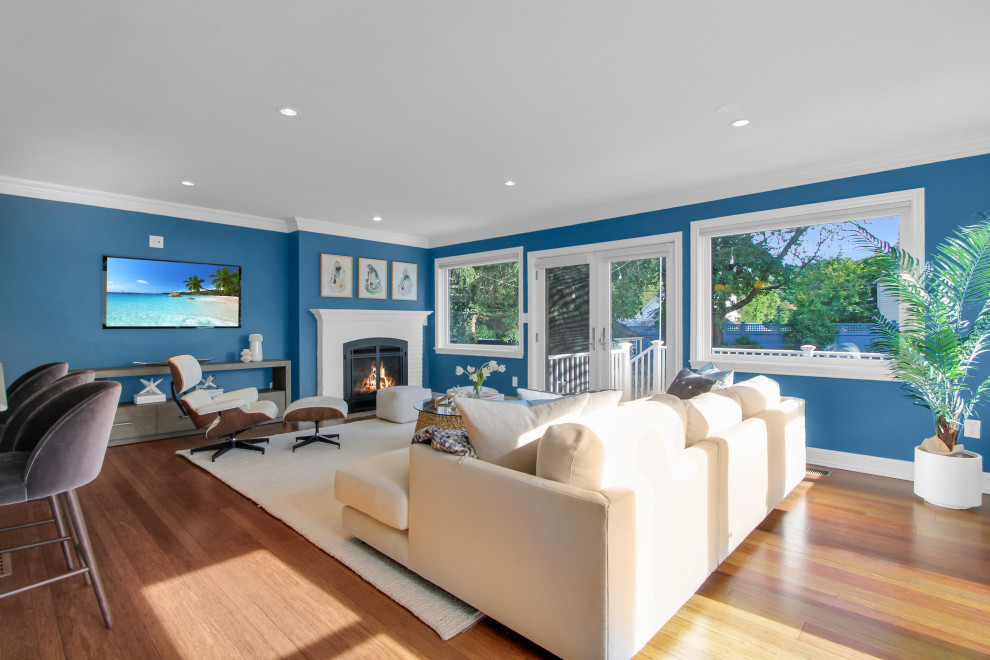 Foto di un soggiorno minimal di medie dimensioni e aperto con pareti blu, pavimento in legno massello medio, camino classico, cornice del camino in mattoni e TV a parete
