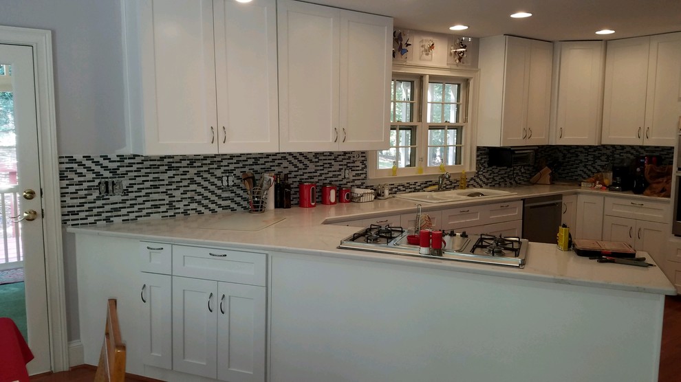 Mid-sized transitional u-shaped medium tone wood floor and brown floor kitchen photo in Atlanta with a drop-in sink, shaker cabinets, white cabinets, solid surface countertops, multicolored backsplash, stone tile backsplash, stainless steel appliances, a peninsula and white countertops