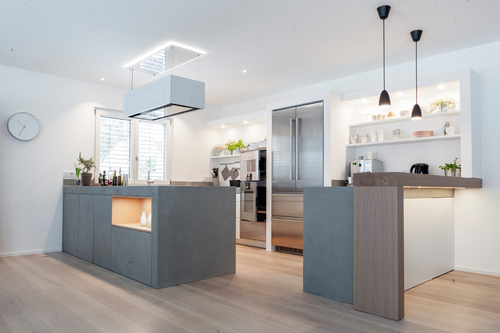 Mid-sized scandinavian u-shaped open plan kitchen in Munich with flat-panel cabinets, grey cabinets, concrete benchtops, stainless steel appliances, light hardwood floors, a peninsula, beige floor and grey benchtop.