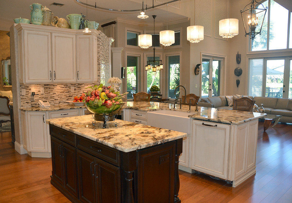 Inspiration for a large transitional medium tone wood floor kitchen remodel in Miami with a farmhouse sink, recessed-panel cabinets, white cabinets, granite countertops, multicolored backsplash, paneled appliances and an island