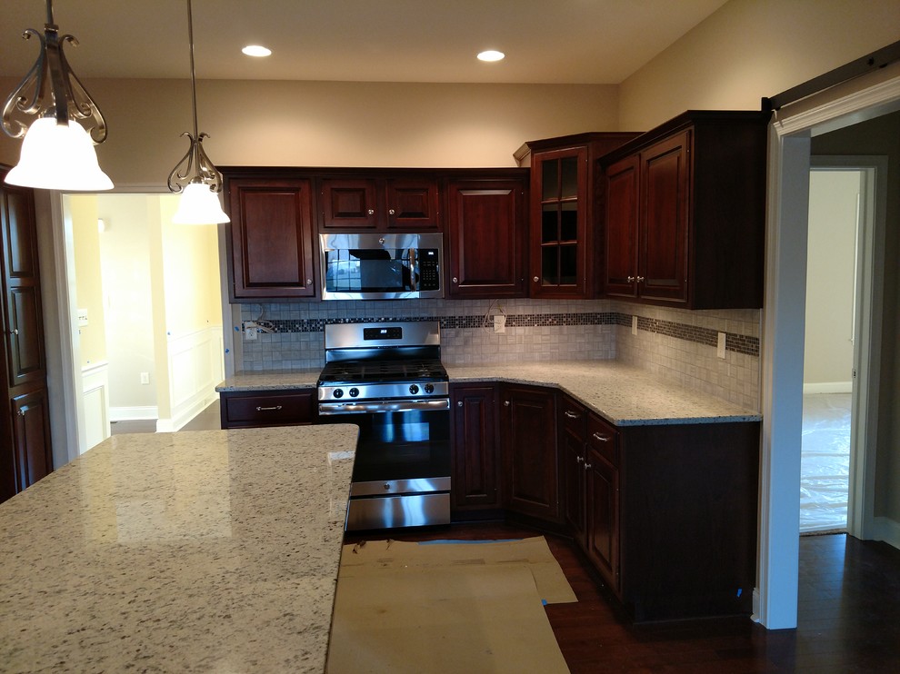 Mid-sized transitional kitchen photo with raised-panel cabinets, dark wood cabinets, quartz countertops, multicolored backsplash, ceramic backsplash, stainless steel appliances and an island