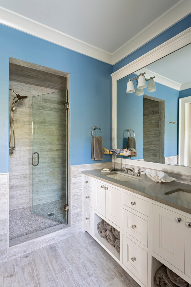 Inspiration for a beach style bathroom in Charleston with recessed-panel cabinets, white cabinets, an alcove shower, gray tile, blue walls, an undermount sink, grey floor, a hinged shower door and grey benchtops.