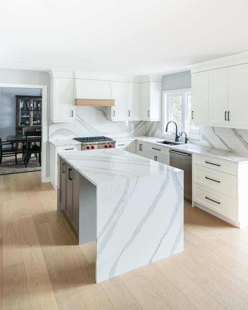 Mid-sized transitional u-shaped light wood floor eat-in kitchen photo in Toronto with an undermount sink, shaker cabinets, white cabinets, quartz countertops, white backsplash, quartz backsplash, stainless steel appliances, an island and white countertops
