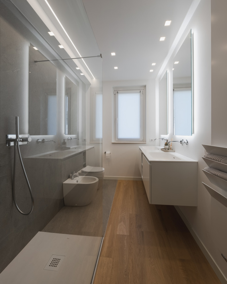 Photo of a mid-sized contemporary 3/4 bathroom in Milan with flat-panel cabinets, white cabinets, an open shower, a two-piece toilet, gray tile, porcelain tile, white walls, light hardwood floors, a drop-in sink, solid surface benchtops, beige floor, white benchtops, a double vanity and a floating vanity.