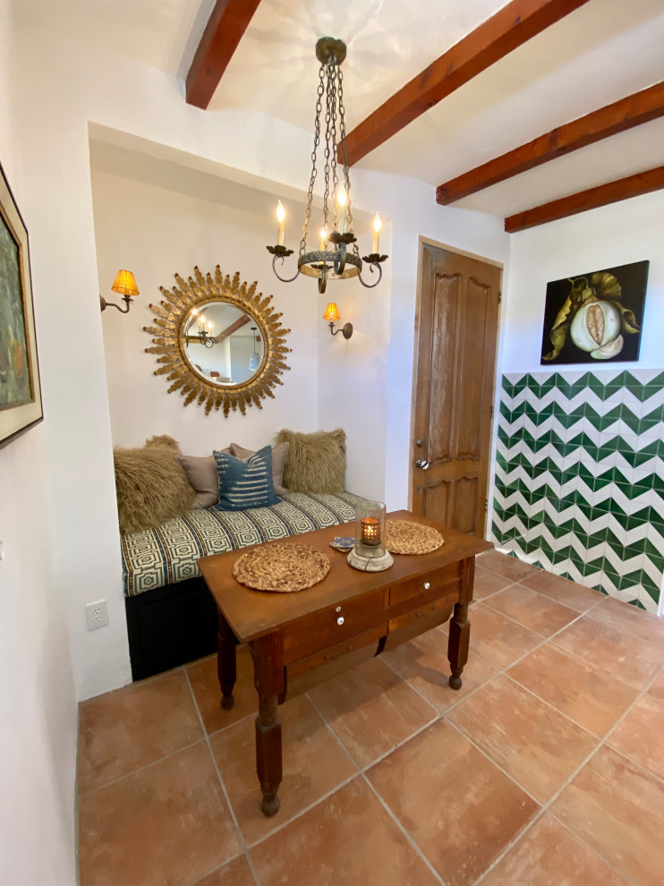 Design ideas for a small mediterranean dining room in San Diego with white walls, porcelain floors, a corner fireplace, a plaster fireplace surround, orange floor and exposed beam.