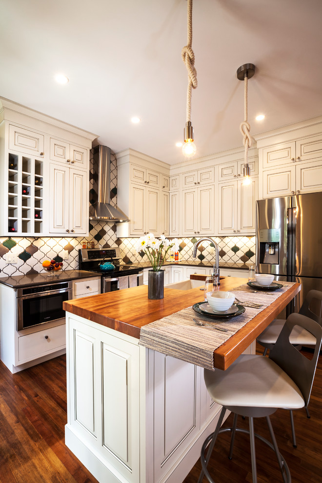 Example of a mid-sized transitional l-shaped medium tone wood floor and brown floor eat-in kitchen design in Denver with a farmhouse sink, raised-panel cabinets, multicolored backsplash, ceramic backsplash, stainless steel appliances, an island, white cabinets and solid surface countertops