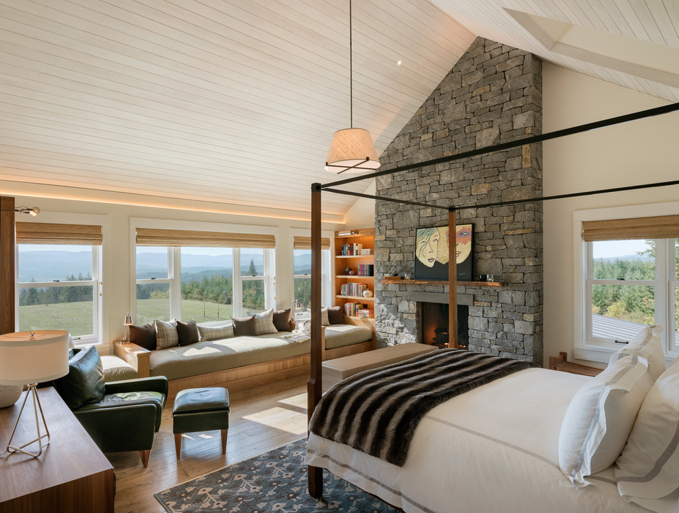 Design ideas for a large country master bedroom in Other with beige walls, medium hardwood floors, a standard fireplace, a stone fireplace surround and brown floor.