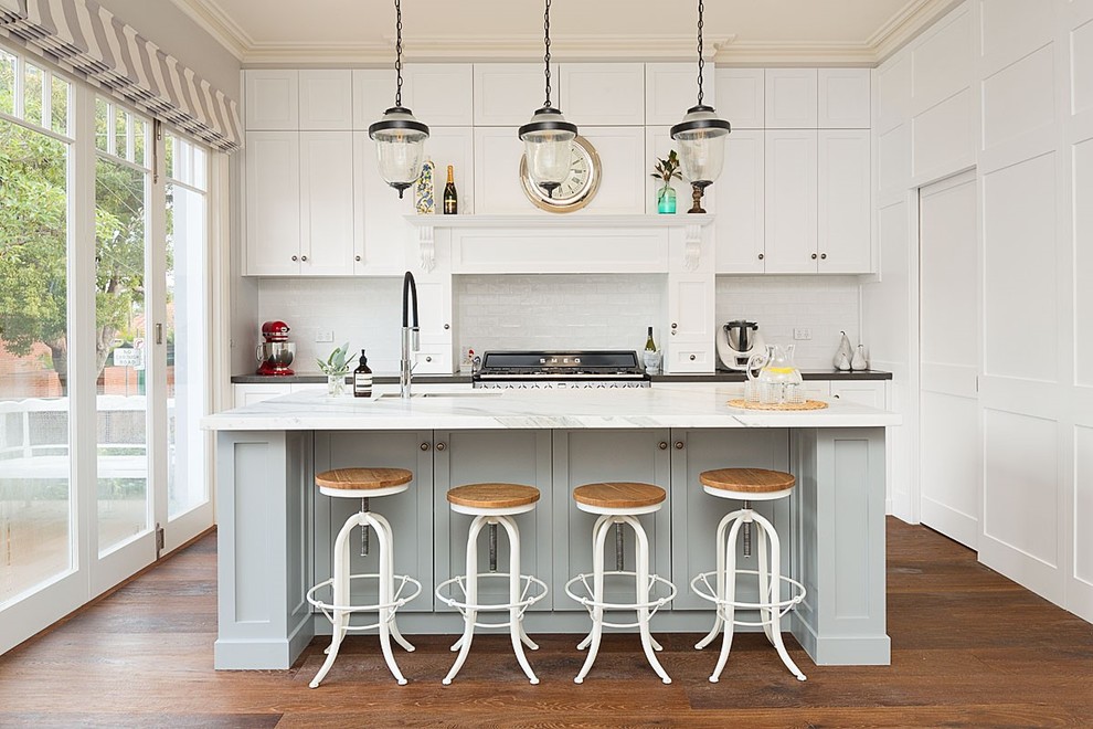 Large traditional galley eat-in kitchen in Sydney with a drop-in sink, shaker cabinets, white cabinets, marble benchtops, white splashback, ceramic splashback, stainless steel appliances, medium hardwood floors, with island and brown floor.