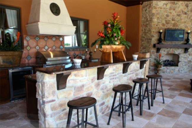 This is an example of a large country backyard patio in Austin with an outdoor kitchen, natural stone pavers and a roof extension.