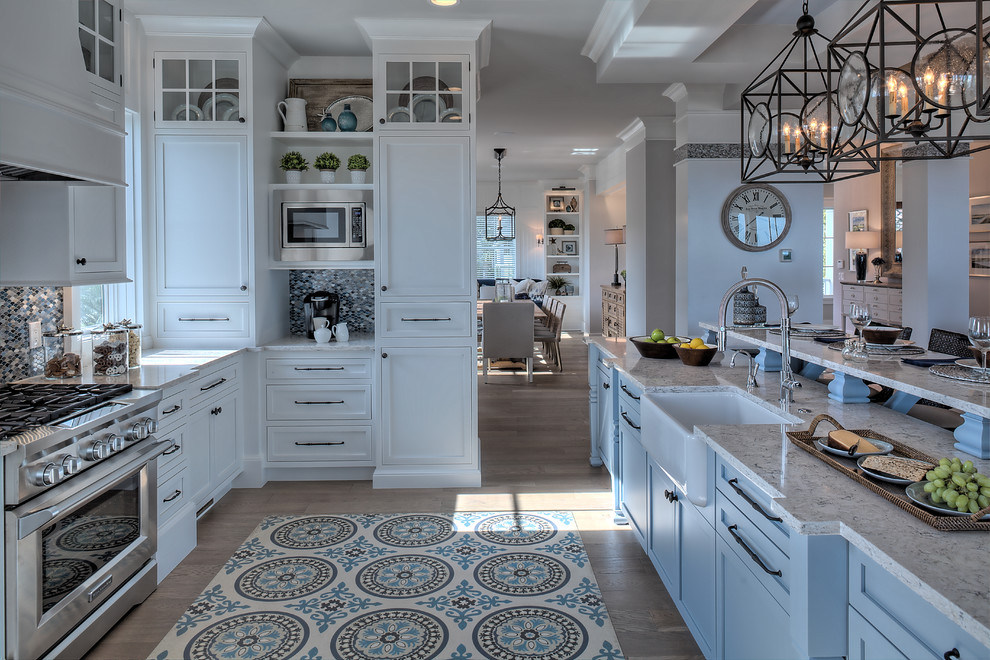 Design ideas for a beach style kitchen in Other with a farmhouse sink, shaker cabinets, white cabinets, multi-coloured splashback, mosaic tile splashback, stainless steel appliances, medium hardwood floors, with island, brown floor and grey benchtop.