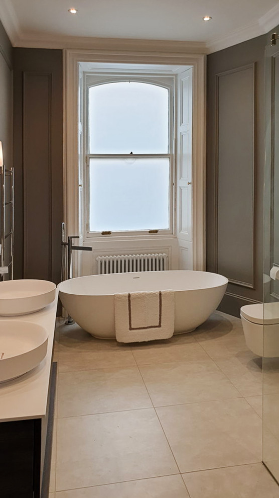This is an example of a mid-sized contemporary master bathroom in Edinburgh with a freestanding tub, an open shower, a double vanity, a floating vanity, beige benchtops, a wall-mount toilet, brown walls, a vessel sink and beige floor.