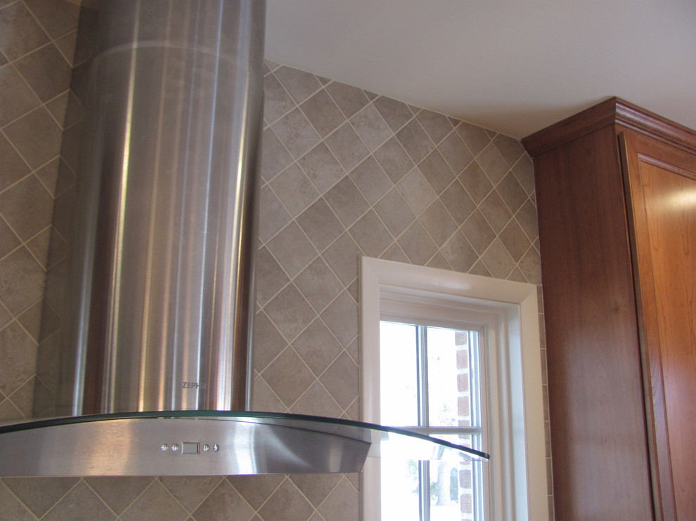 Example of a large classic single-wall home design design with raised-panel cabinets, medium tone wood cabinets, granite countertops, gray backsplash, porcelain backsplash, stainless steel appliances and an island