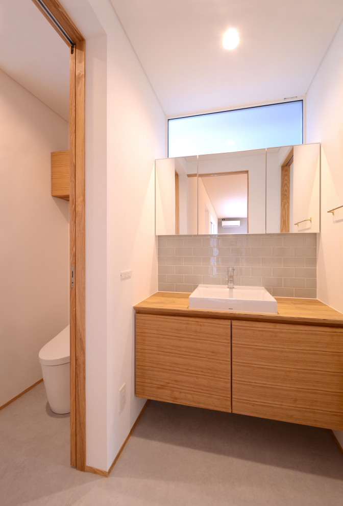 Medium sized modern cloakroom with freestanding cabinets, medium wood cabinets, a one-piece toilet, white tiles, porcelain tiles, white walls, limestone flooring, a vessel sink, wooden worktops, beige floors, a built in vanity unit, a wallpapered ceiling and wallpapered walls.