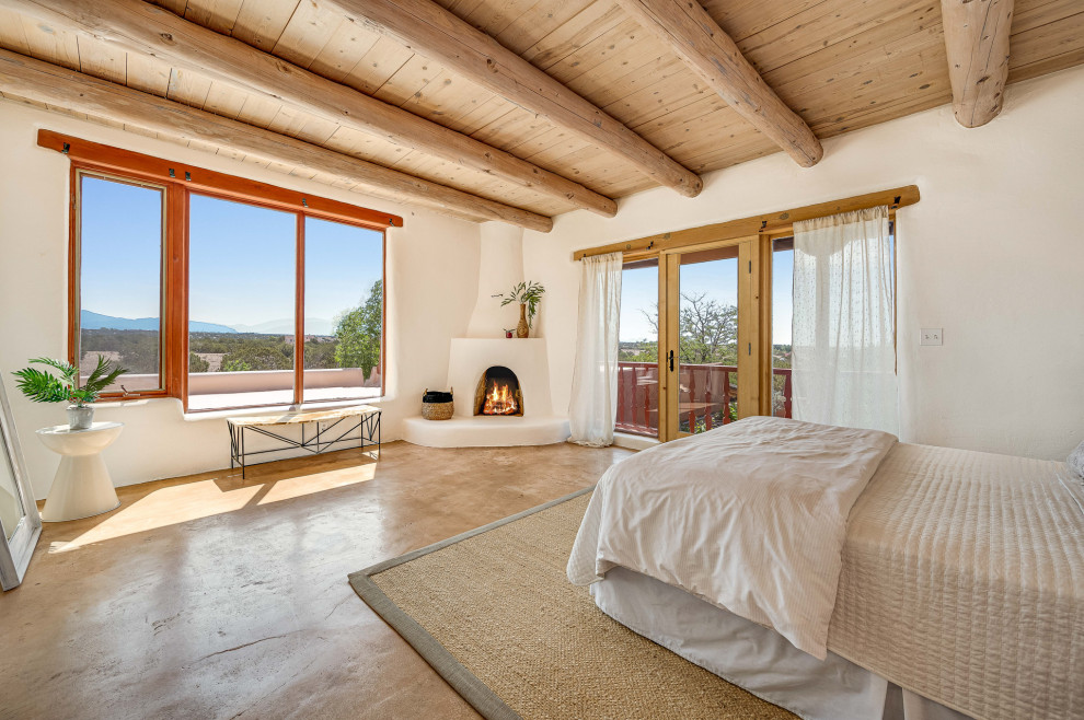 Photo of a large master bedroom in Other with white walls, concrete floors, a corner fireplace, a plaster fireplace surround, beige floor and exposed beam.