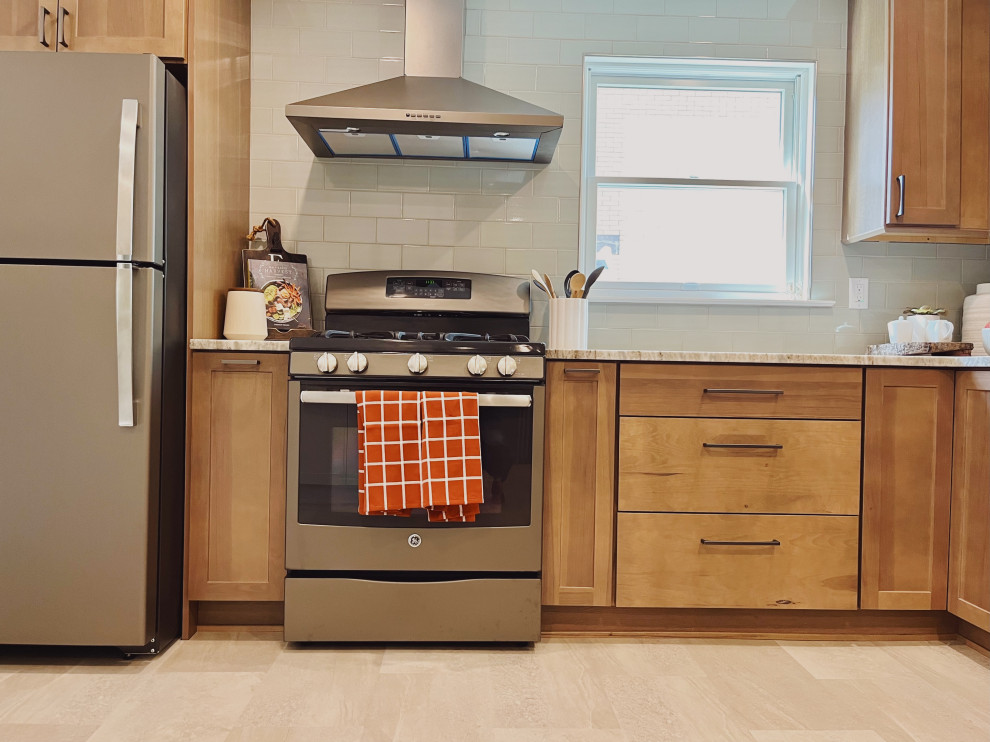 Mid-sized transitional l-shaped vinyl floor and beige floor eat-in kitchen photo with a farmhouse sink, shaker cabinets, medium tone wood cabinets, quartzite countertops, green backsplash, ceramic backsplash, stainless steel appliances, no island and beige countertops