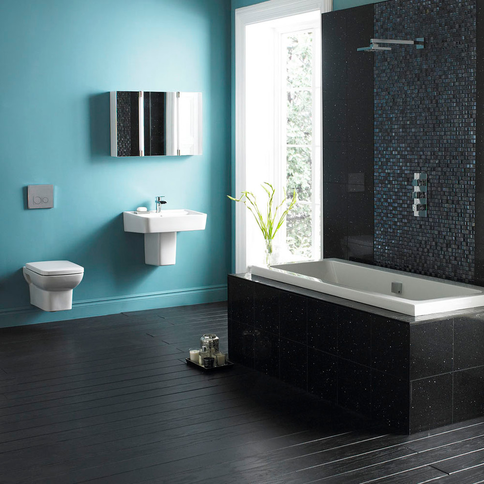 This is an example of a contemporary bathroom in Other with a wall-mount sink, a drop-in tub, a shower/bathtub combo, a wall-mount toilet, black tile, blue walls and painted wood floors.