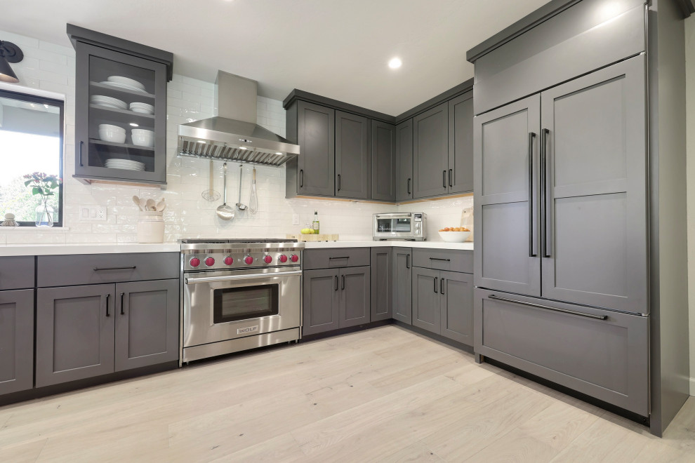 Example of a mid-sized transitional l-shaped laminate floor open concept kitchen design with a double-bowl sink, flat-panel cabinets, gray cabinets, quartz countertops, white backsplash, ceramic backsplash, stainless steel appliances, an island and white countertops