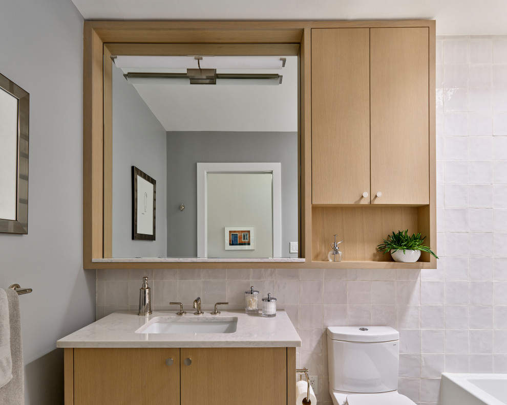 Стильный дизайн: маленькая детская ванная комната в современном стиле с плоскими фасадами, светлыми деревянными фасадами, ванной в нише, раздельным унитазом, белой плиткой, керамогранитной плиткой, белыми стенами, полом из керамогранита, врезной раковиной, столешницей из искусственного кварца, бежевым полом, белой столешницей, тумбой под одну раковину и встроенной тумбой для на участке и в саду - последний тренд