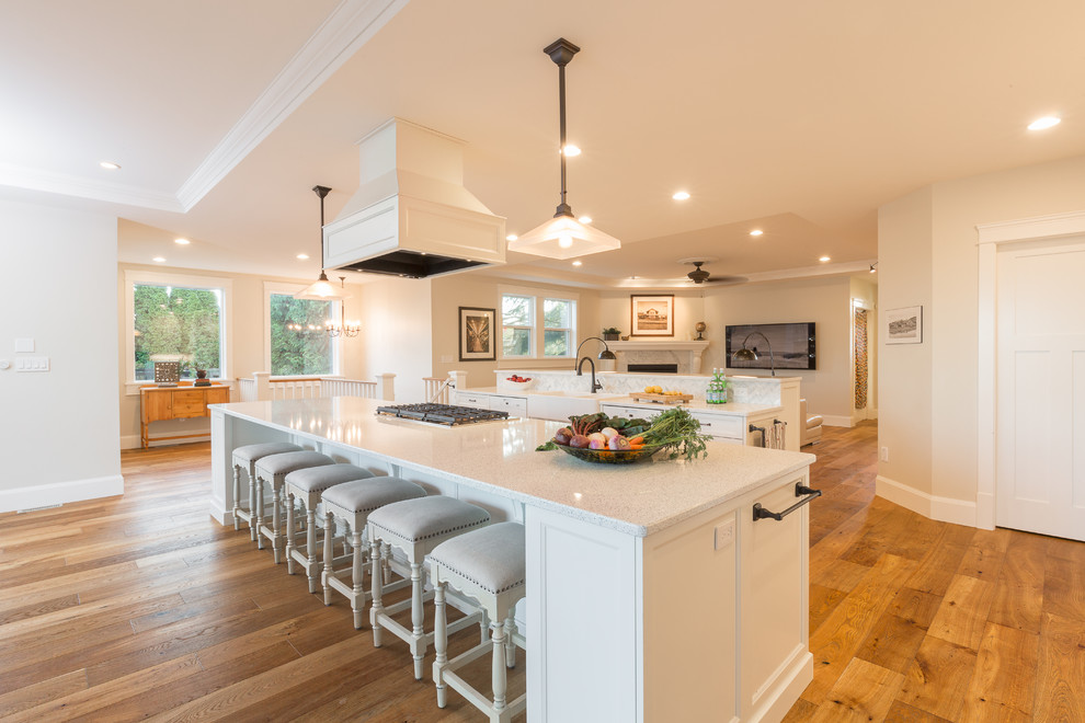 Inspiration for a traditional galley open plan kitchen in Vancouver with a farmhouse sink, recessed-panel cabinets, white cabinets, quartzite benchtops, white splashback, white appliances, light hardwood floors and multiple islands.