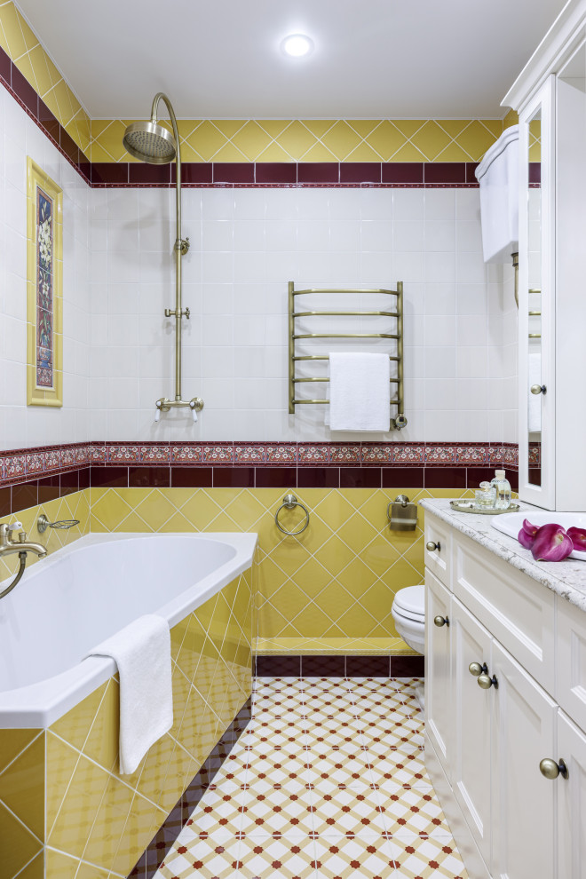 This is an example of a mid-sized traditional master bathroom in Moscow with recessed-panel cabinets, beige cabinets, a corner tub, a shower/bathtub combo, yellow tile, ceramic tile, beige walls, porcelain floors, a drop-in sink, engineered quartz benchtops, multi-coloured floor, an open shower, beige benchtops, an enclosed toilet, a single vanity and a freestanding vanity.