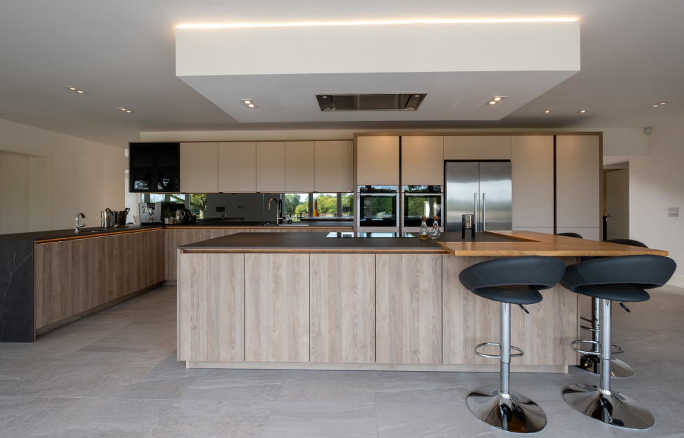 Inspiration for a large contemporary l-shaped open plan kitchen in Hampshire with flat-panel cabinets, white cabinets, grey splashback, glass sheet splashback, porcelain floors, with island, multi-coloured floor and grey benchtop.