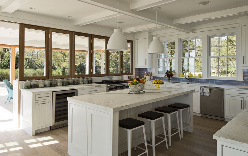 Design ideas for a beach style u-shaped kitchen in New York with an undermount sink, shaker cabinets, white cabinets, blue splashback, subway tile splashback, stainless steel appliances, dark hardwood floors and with island.