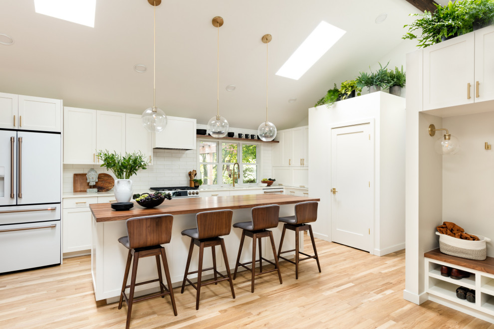 Design ideas for a mid-sized scandinavian l-shaped eat-in kitchen in Seattle with an undermount sink, recessed-panel cabinets, white cabinets, quartz benchtops, white splashback, subway tile splashback, white appliances, light hardwood floors, with island, white benchtop and vaulted.