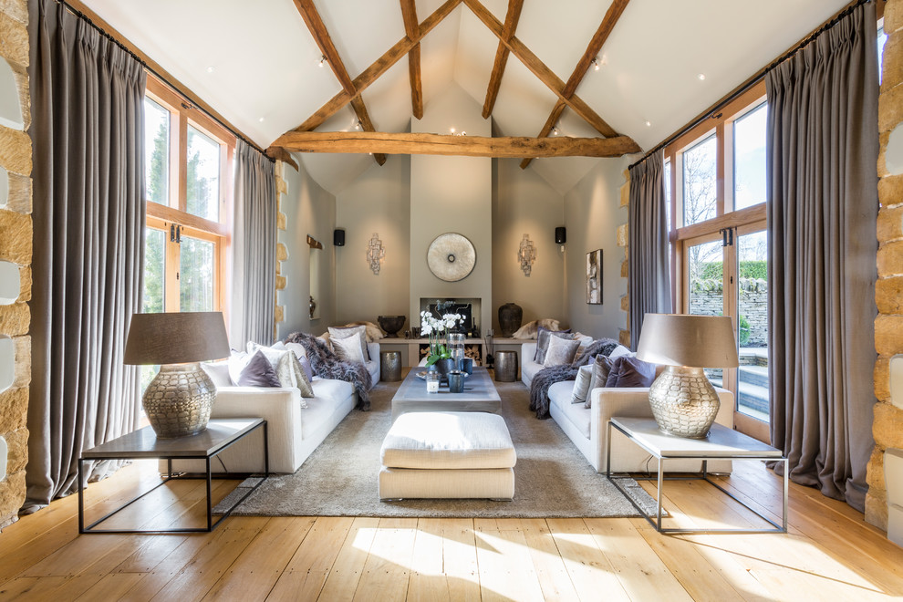 This is an example of a mid-sized country formal open concept living room in Gloucestershire with grey walls, light hardwood floors, a wood stove and beige floor.