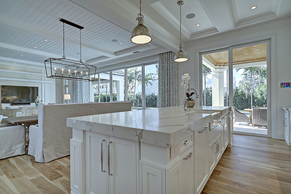Large beach style single-wall open plan kitchen in Miami with a farmhouse sink, recessed-panel cabinets, white cabinets, marble benchtops, white splashback, subway tile splashback, panelled appliances, light hardwood floors and with island.