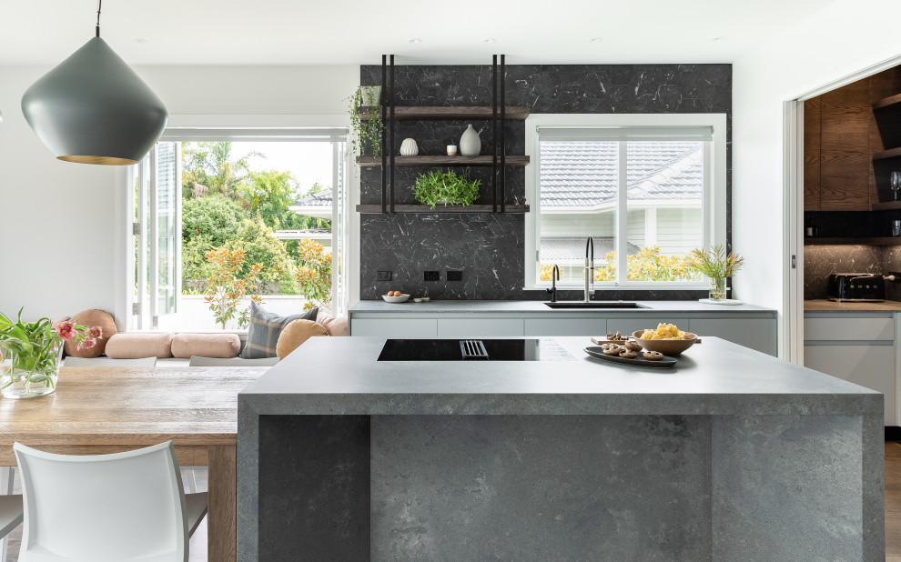 Design ideas for a mid-sized contemporary galley eat-in kitchen in Auckland with a single-bowl sink, flat-panel cabinets, grey cabinets, quartz benchtops, black splashback, porcelain splashback, dark hardwood floors, with island, brown floor and grey benchtop.